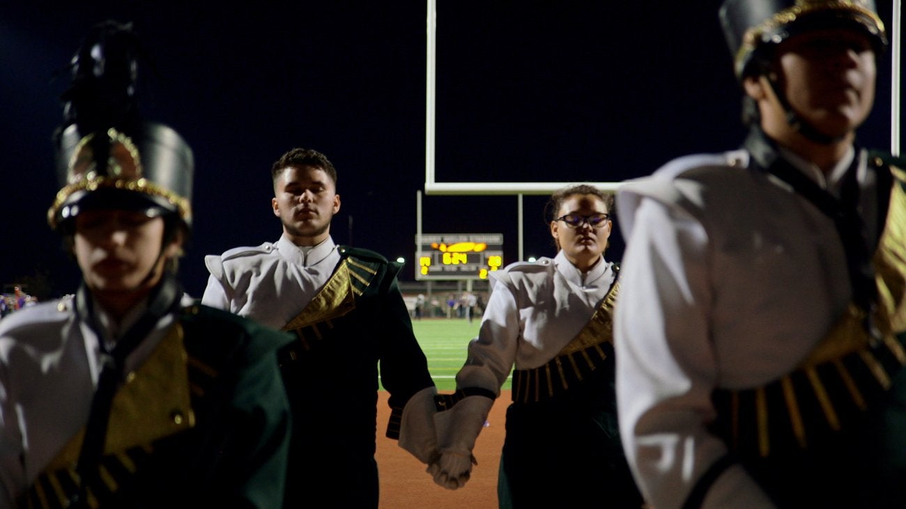 Image of high school marching band, holding hands, eyes closed and breathing before they perform.