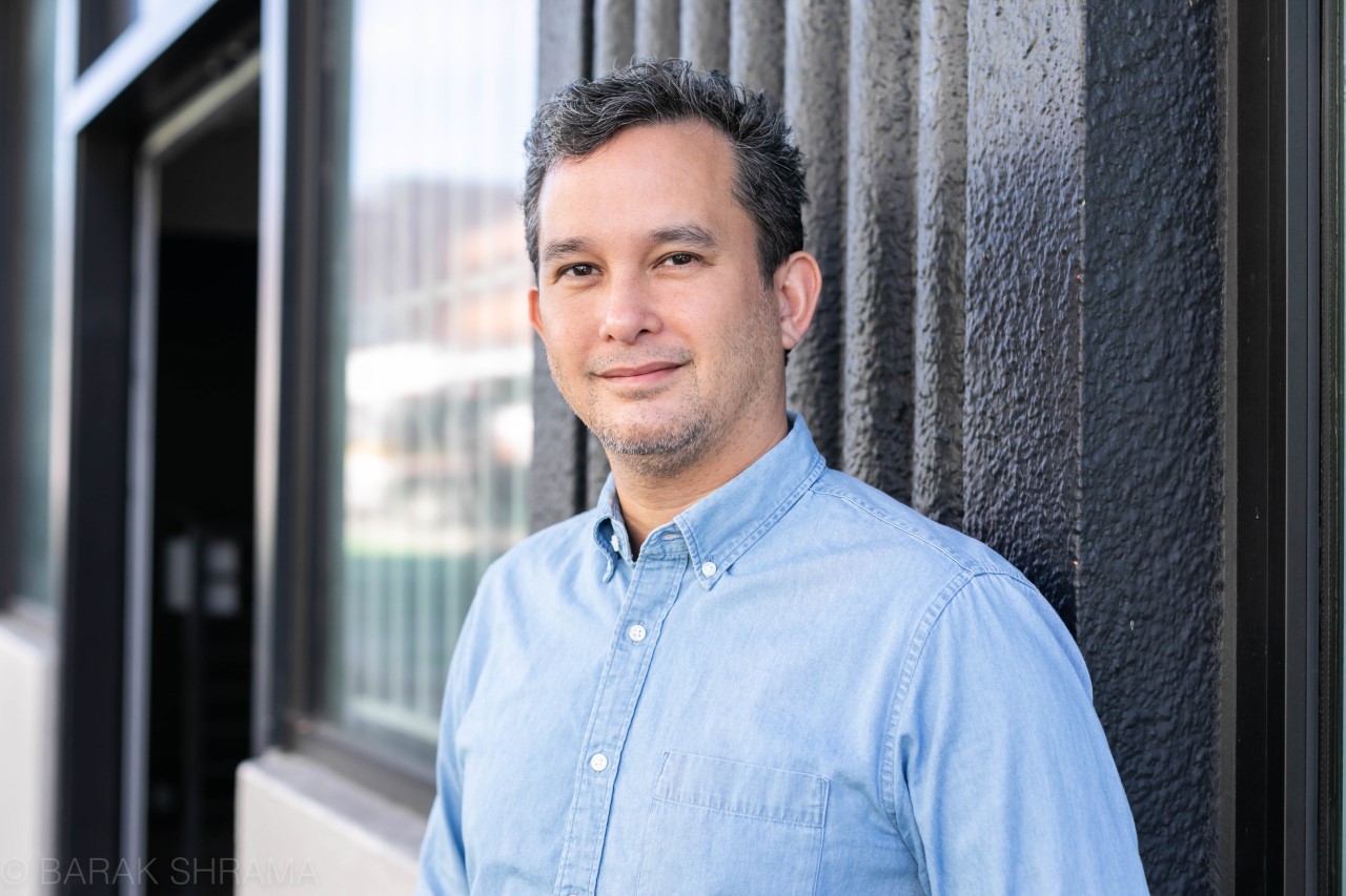 A man with short dark hair wearing a blue shirt smiles at the camera