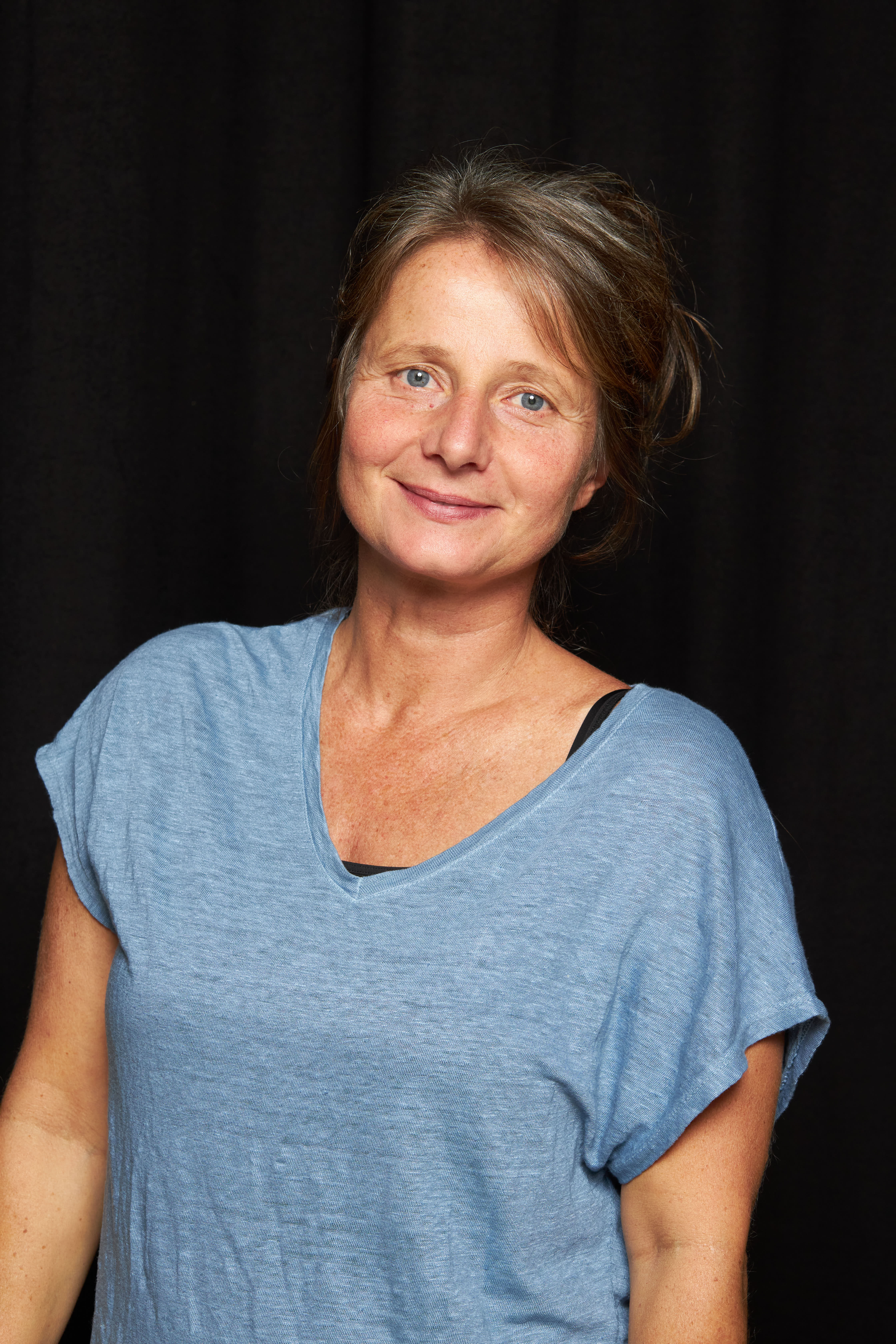 Woman with short brown hair smiling at camera, wearing blue tshirt