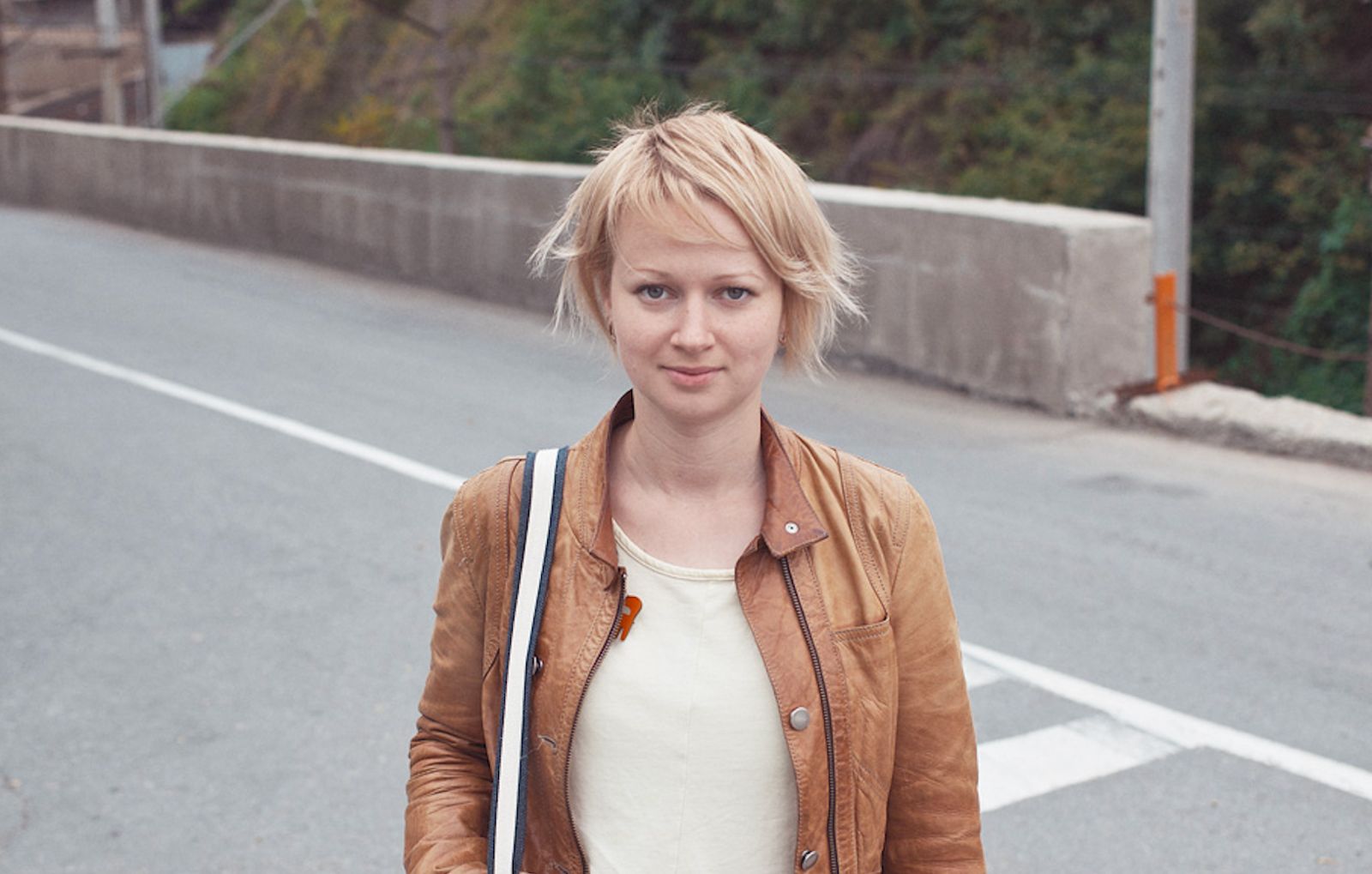 Woman with short blonde hair and a brown jacket looks at the camera