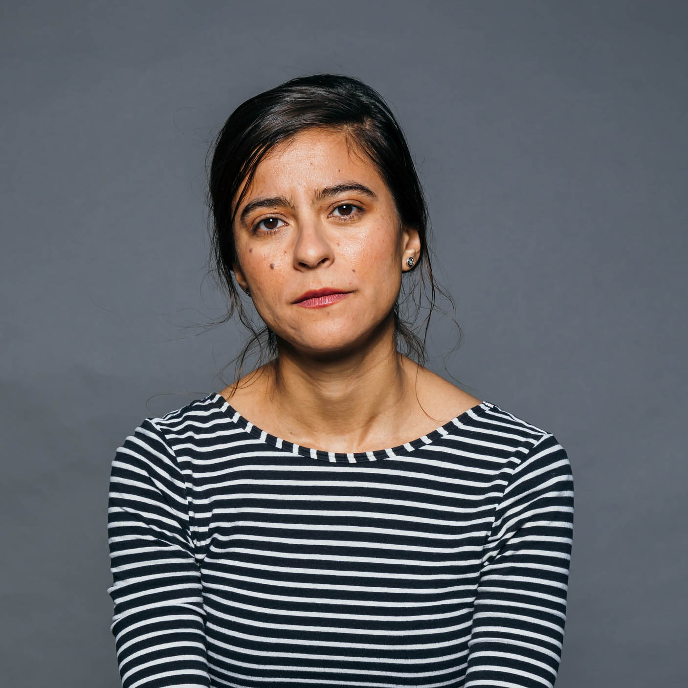 Photo of director Andrea Patiño Contreras. Woman with brown hair wearing a black and white striped shirt 