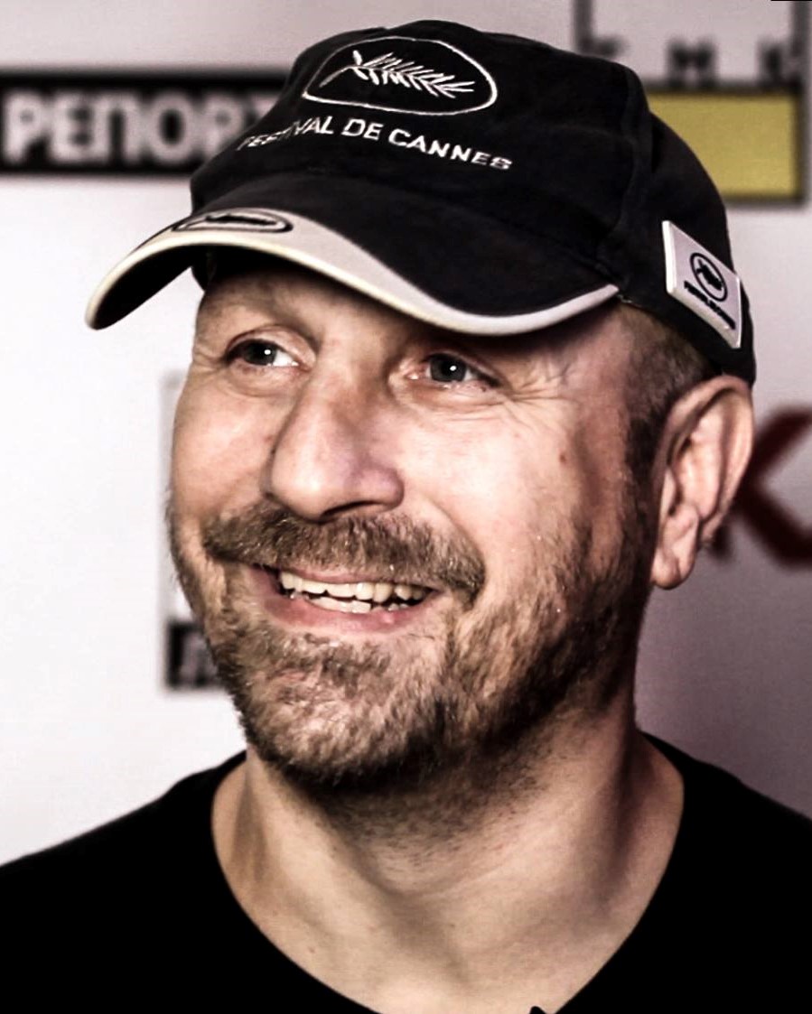 Man smiling with facial hair and wearing a baseball cap