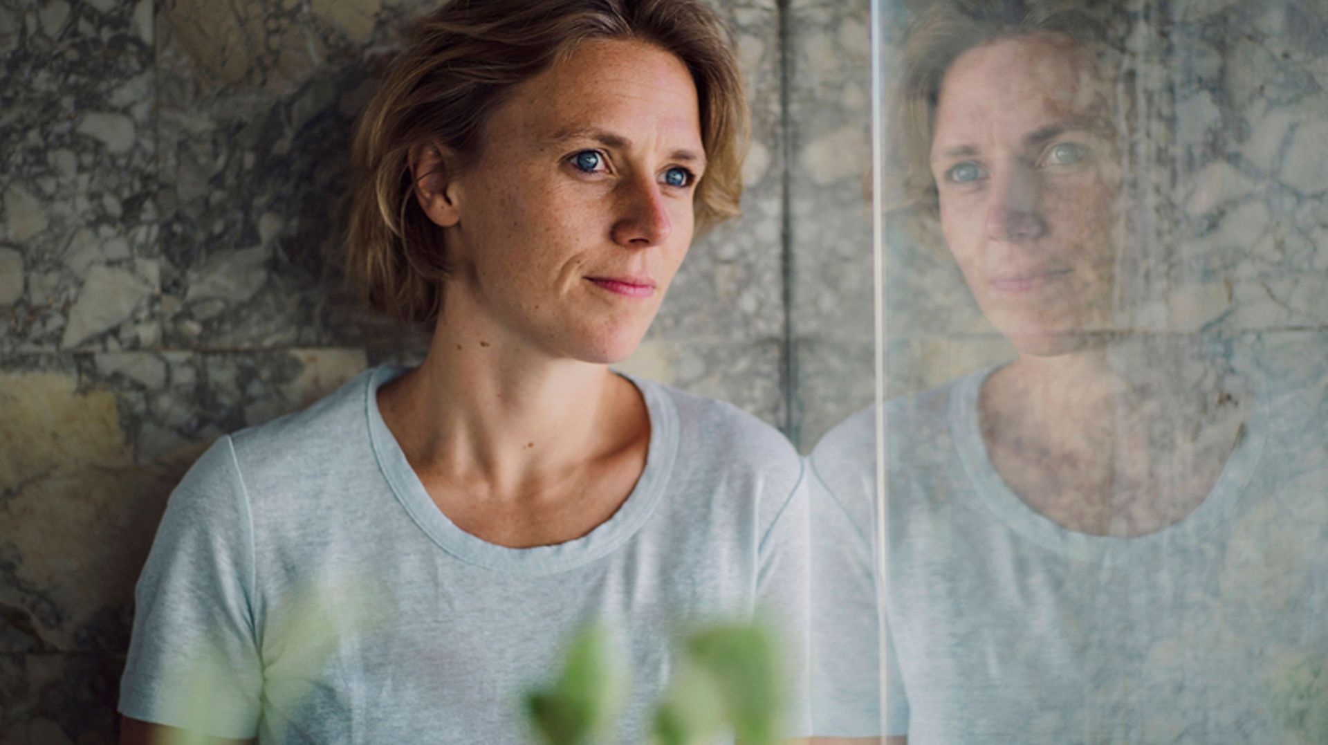 Woman wearing a white top stares out of the window, her face is reflected back