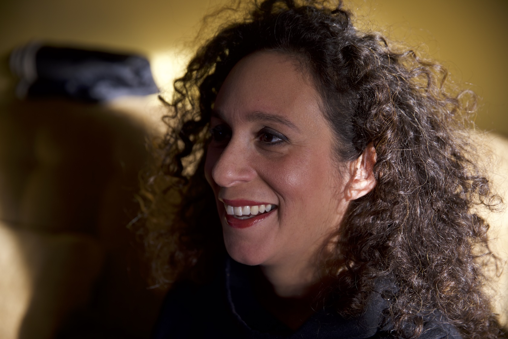 Close up of woman smiling with curly brown hair, looking away from camera