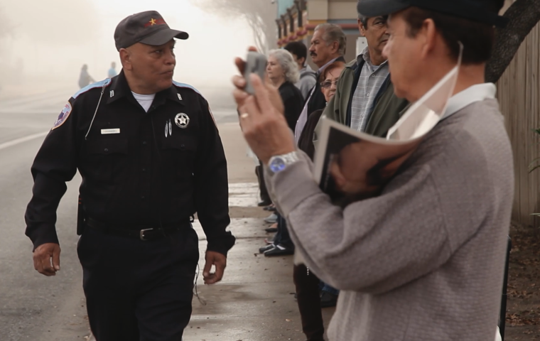 Photo of Latino man, a security guard looking at a crowd of anti-Abortion activists. 