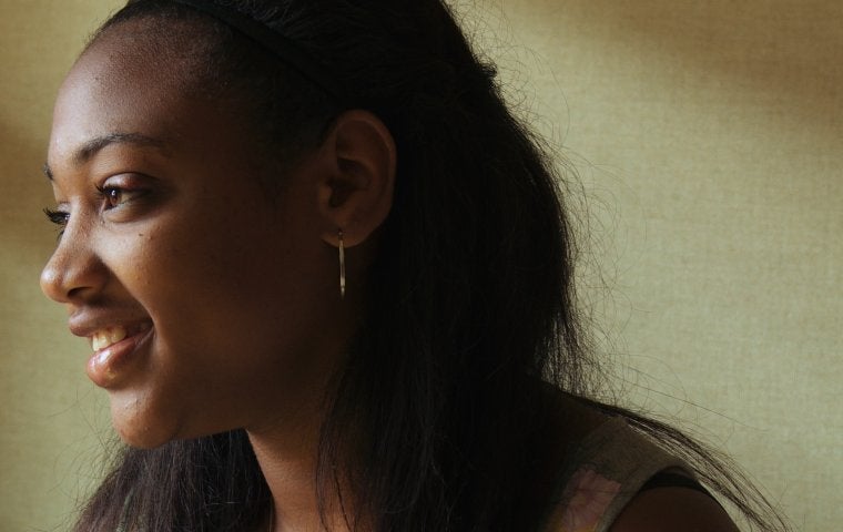 Photograph of a Black teenage girl with hair pulled back from her face, looking to the left smiling. 