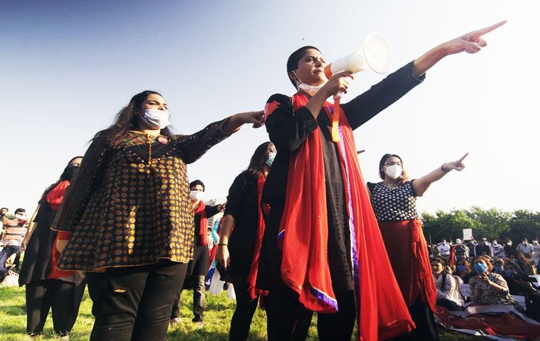 Image of Pakistani women pointing fingers, wearing orange scarved with megaphoone.