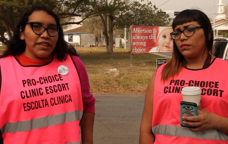 Two sisters wear pink vests reading "Clinic Escort" 