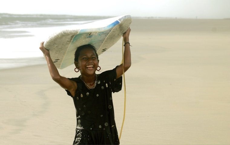 Girl smiling holding a surf board on her head 