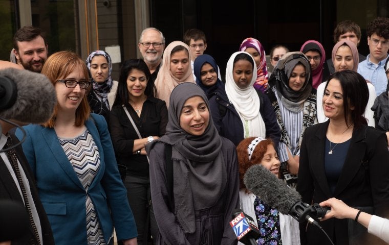 Photo of a crowd and a press conference, with a woman in front speaking with a Hijab.