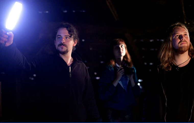 Two men and a woman standing in the dark illuminated by a light held out in front of them