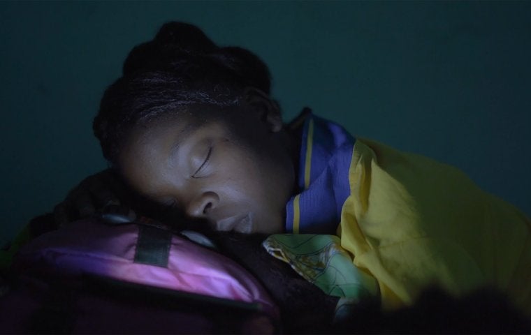 Photo of African woman sleeping on a pink pillow, with light coming from a mobile device