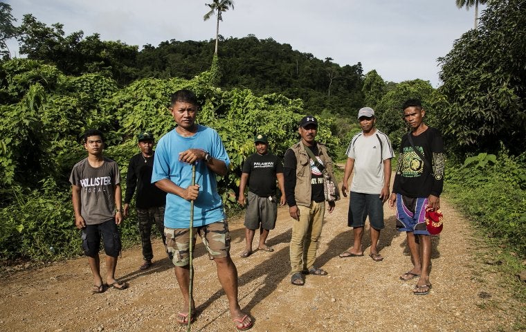 Photo of a group of people in tshirts and shorts, standing in a jungle path looking at camera. 