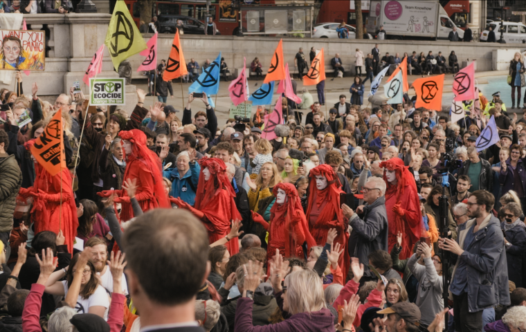 Protest in Trafalgar Square with colorful flags waving. Group of people draped in red cloths walking through the crowd