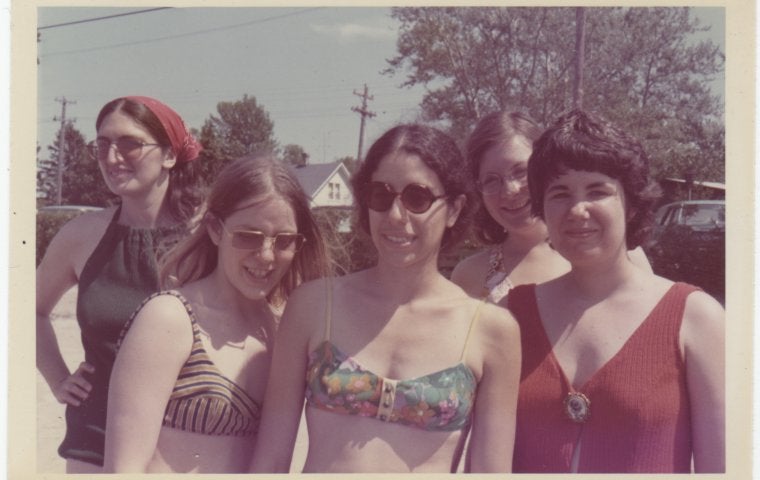 Image from the 1960s of a group of young white women in bikinis and sunglasses smiling at camera