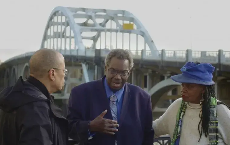 Image of three African American elders, in front of a bridge talking.  