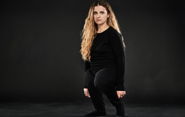 Image of filmmaker Ella Glending. Standing in front of a black background, wearing black shirt and black pants. 