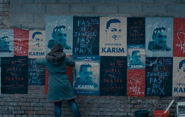 A wall of posters with text in French reading "Justice for Karim" and illustrated image of a young man