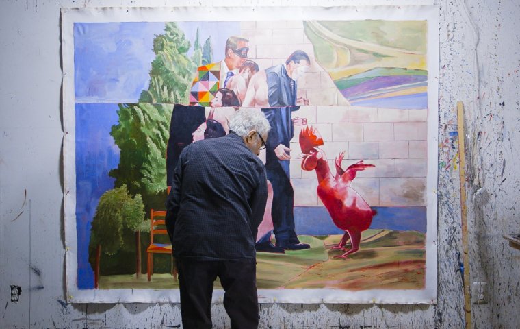 An artist, male, faces a large canvas on which an abstract, colorful piece of art is in-progress
