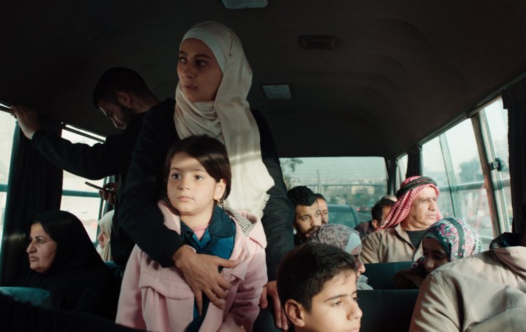 Woman in white headscarf on a bus hugs her daughter standing in front of her