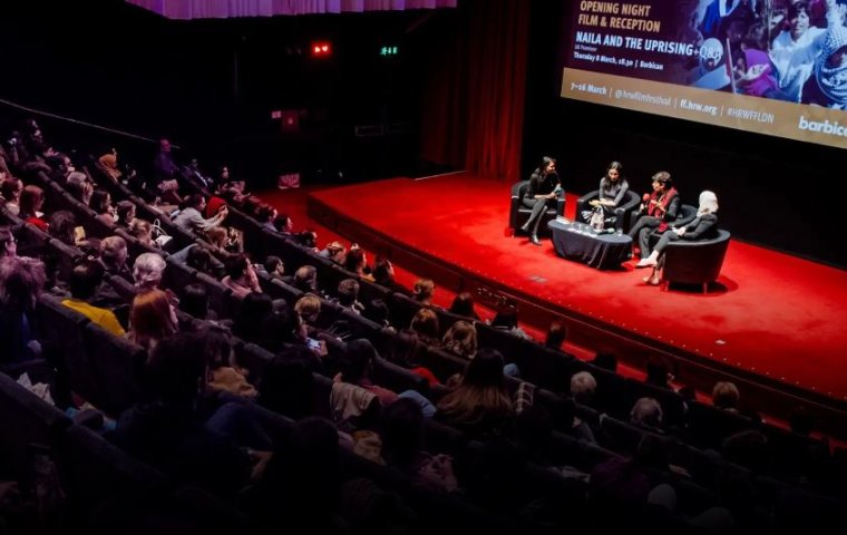 A theater audience watches a panel discussion on stage