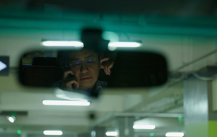 Maria Reza on her phone, reflected in car rearview mirror