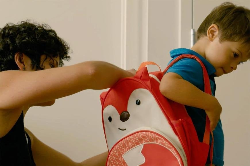 Image of a mom putting a small backpack on her 3 yr old son as he gets ready for school. 