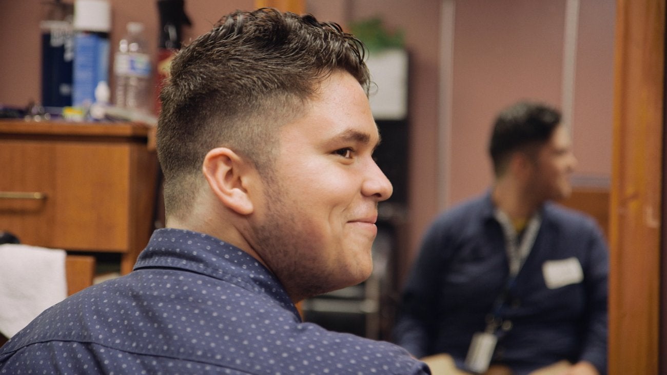Photo of a young man getting his hair cut at a salon and smiling from the side.