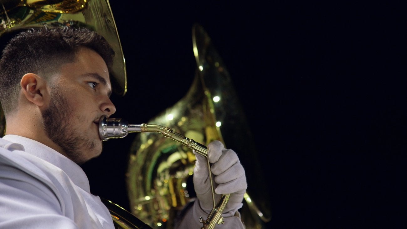 Image of teen boy playing tuba in marching band.
