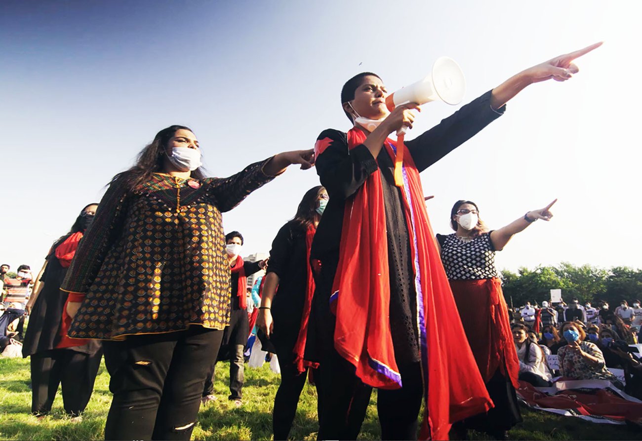 Image of Pakistani women pointing fingers, wearing orange scarved with megaphoone.