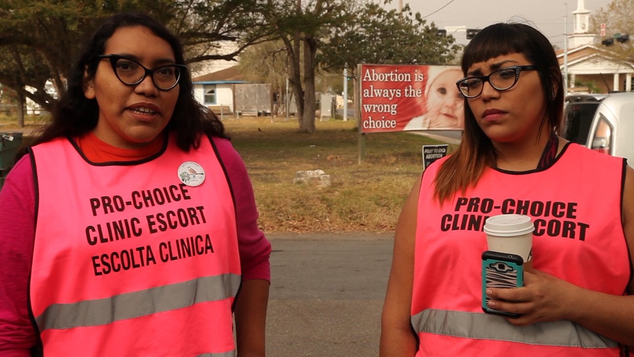 Two sisters wear pink vests reading "Clinic Escort" 