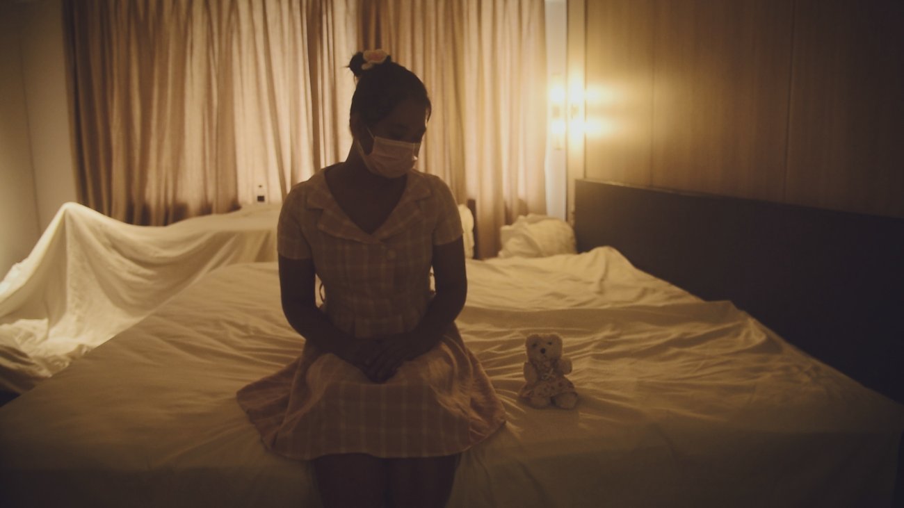 Woman on a bed in dimly lit bed looking at a teddy bear. 