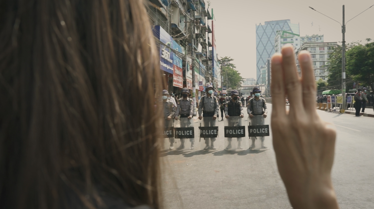 Woman standing in front of police holding three fingers up in protest