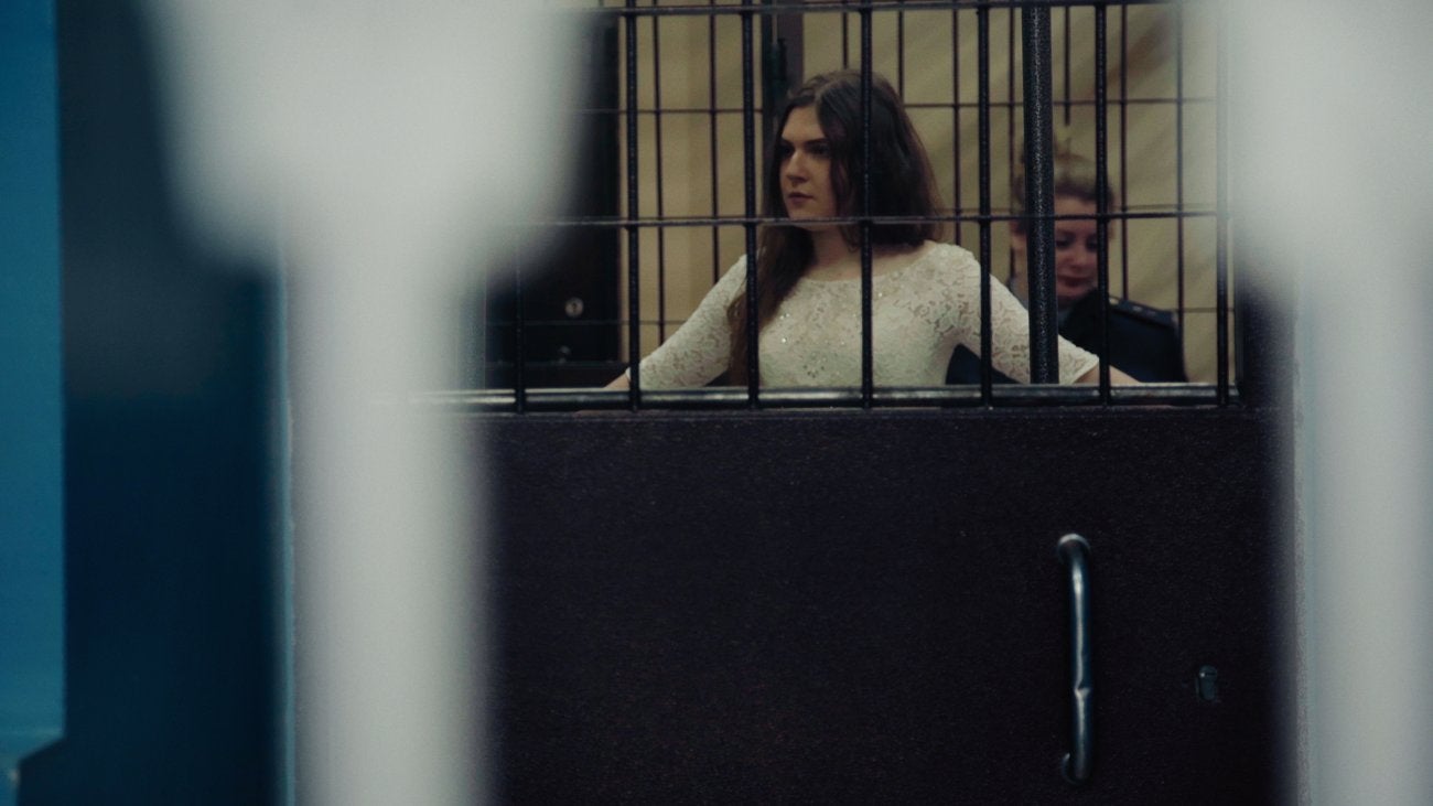 Photo of teenage girl in white sequined dress behind bars during trial in Russia. 