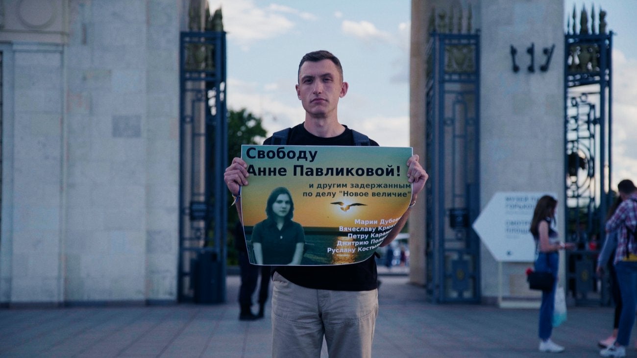 Photo of a young Russian man holding a poster with the image of the teenage girl imprisoned in Russia for her political views