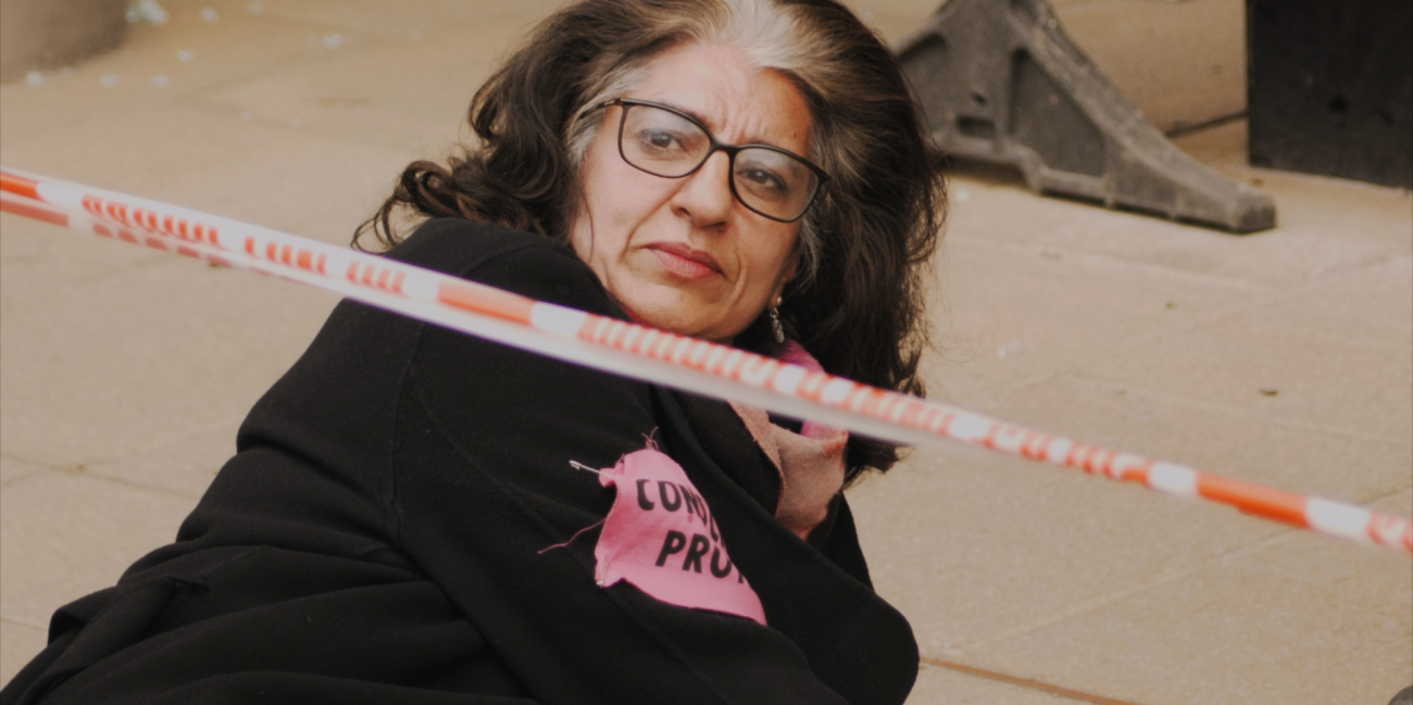 Photo of activist, Farhana lying on the ground wearing a black hooded sweatshirt with pink patch on her arm. 