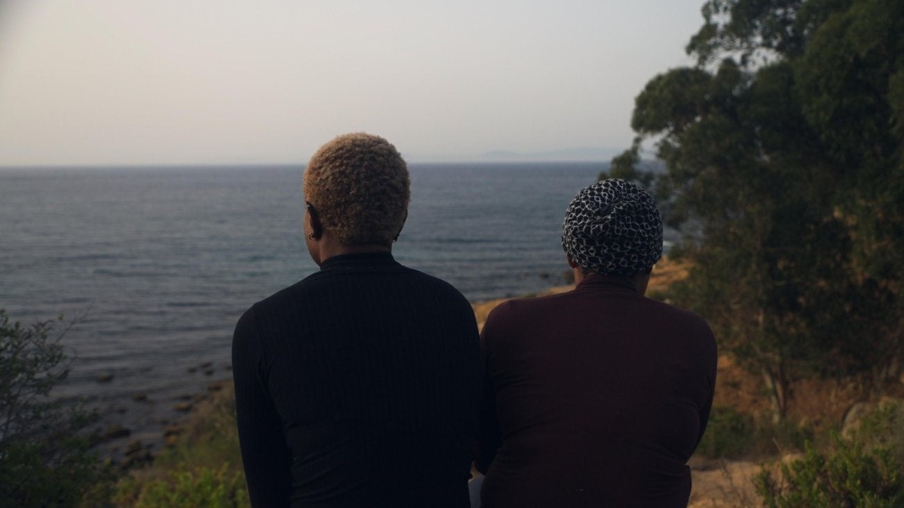 Photo of two young women looking at the sea, taken from the back. 