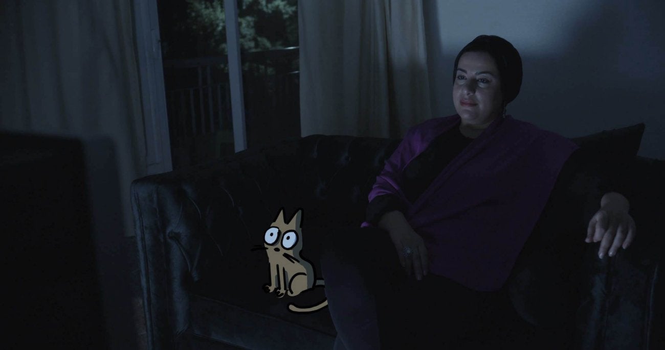 Illustrated image of artist Doaa el-Adl sitting on a couch in the dark, lit by a television, with a drawn cat sitting next to her.