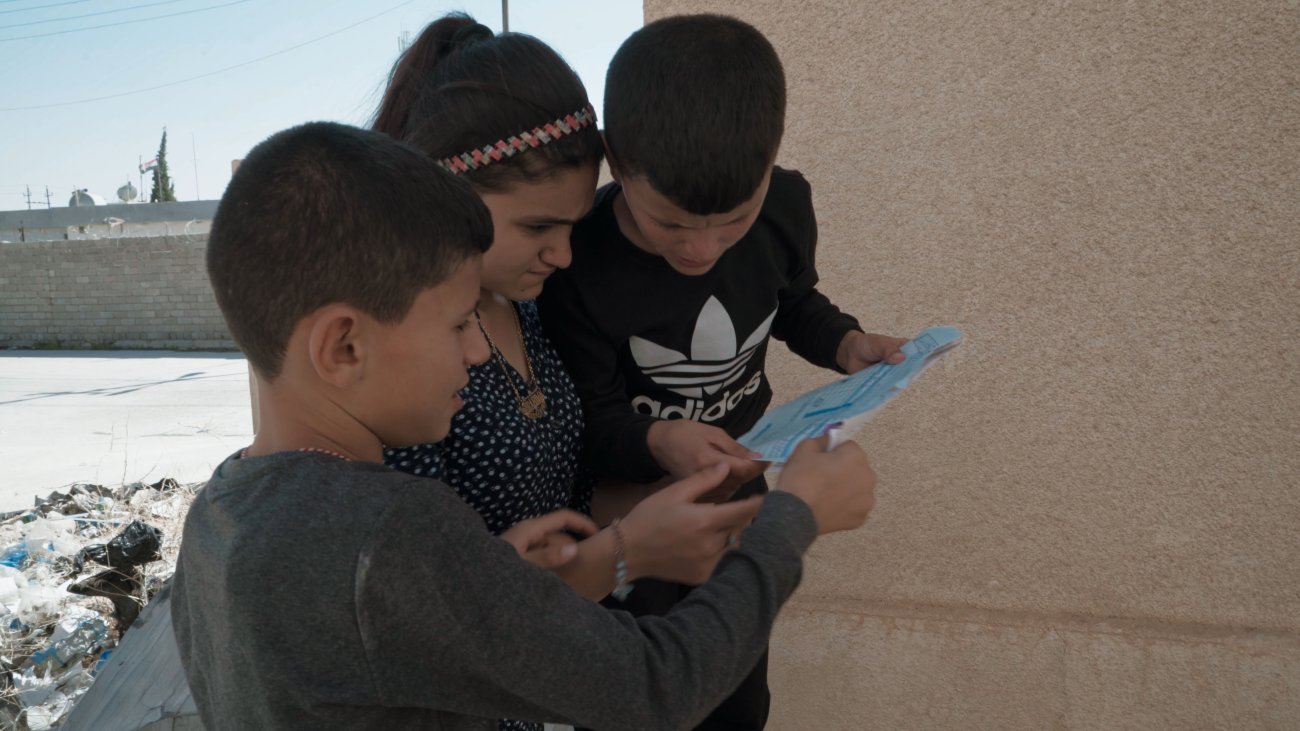 2 boys and a girl gather round a piece of paper, reading it