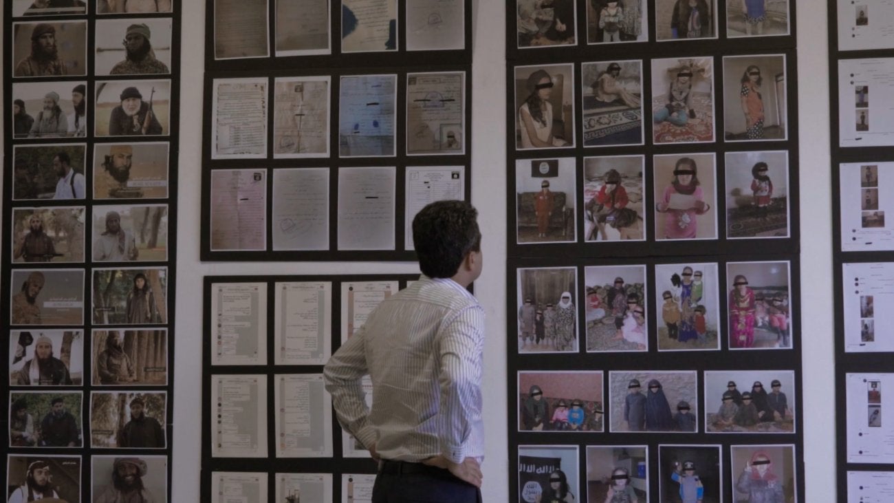 back of a man looking at a wall covered in frames photos of people