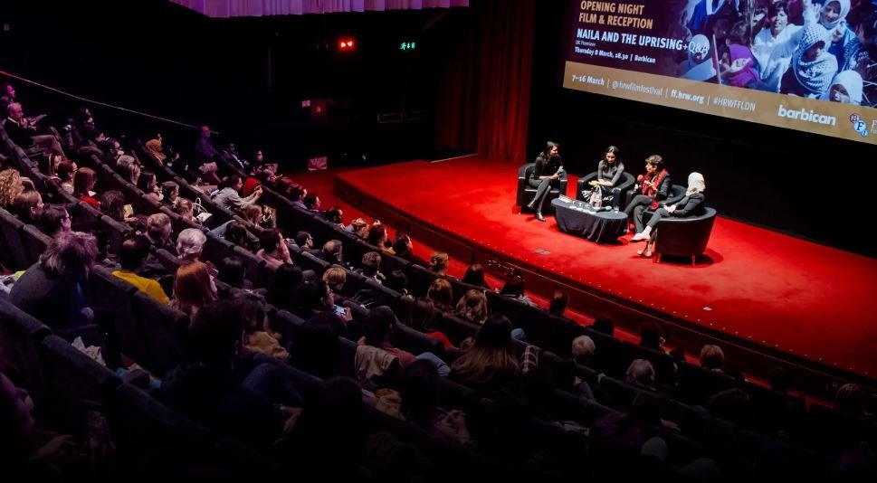 A theater audience watches a panel discussion on stage