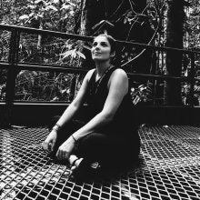 Woman with short hair sitting on the ground smiling and holding her knees.