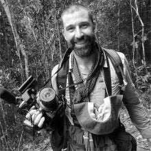 Black and white photo of man in forest holding a camera