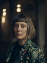 Photo of director Steffi Niederzoll, A white woman with short brown hair and bangs looks over her shoulder towards camera.