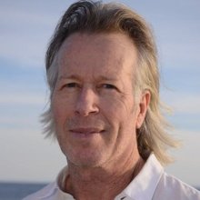 Headshot of man with long white hair swept back wearing a white collared shirt