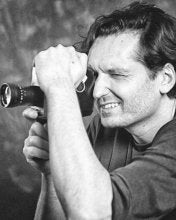 Black and white photo of a man looking through a camera lens