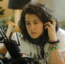 Image of person with long brown curly hair and white skin, holding headphones up to their ears. 